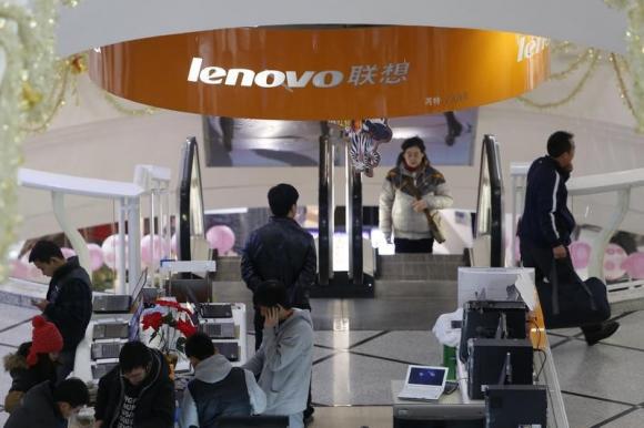 People stand under a sign showing the Lenovo company at a computer market in Shanghai